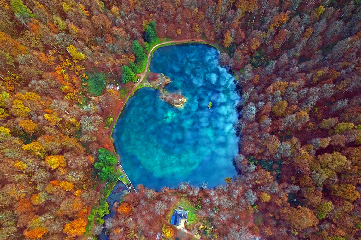 Lac de Bethmale, heart-shaped lake surrounded by autumn-colored forest; photo by Velion X, Unsplash.