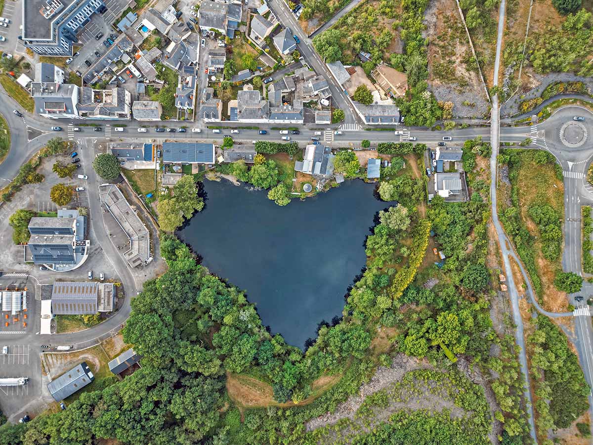 Le Buisson, heart-shaped quarry lake in Trélazé, France, surrounded by urban vegetation, town buildings and roads; photo by Adrien, Unsplash.