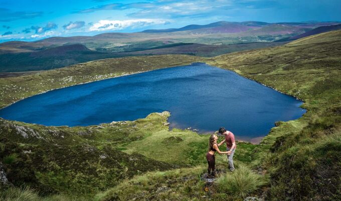 A romantic couple embracing with Lough Ouler, Ireland's heart-shaped lake in the background; photo by Dannii Coughlan, Unsplash.