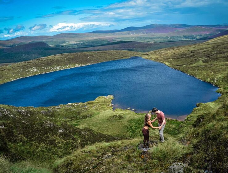 A romantic couple embracing with Lough Ouler, Ireland's heart-shaped lake in the background; photo by Dannii Coughlan, Unsplash.