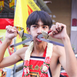 A young man, ma song participant of the Phuket Vegetarian Festival, his cheeks pierced with swords, standing ready for the procession from the Lim Hu Tai Su Shrine, Thailand; photo by Ivan Kralj.
