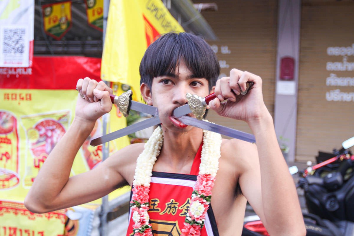 A young man, ma song participant of the Phuket Vegetarian Festival, his cheeks pierced with swords, standing ready for the procession from the Lim Hu Tai Su Shrine, Thailand; photo by Ivan Kralj.