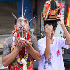 Ma song participant of the Phuket Vegetarian Festival, his face heavily pierced with spikes, standing by the road during the procession of the Lim Hu Tai Su Shrine, Thailand; photo by Ivan Kralj.