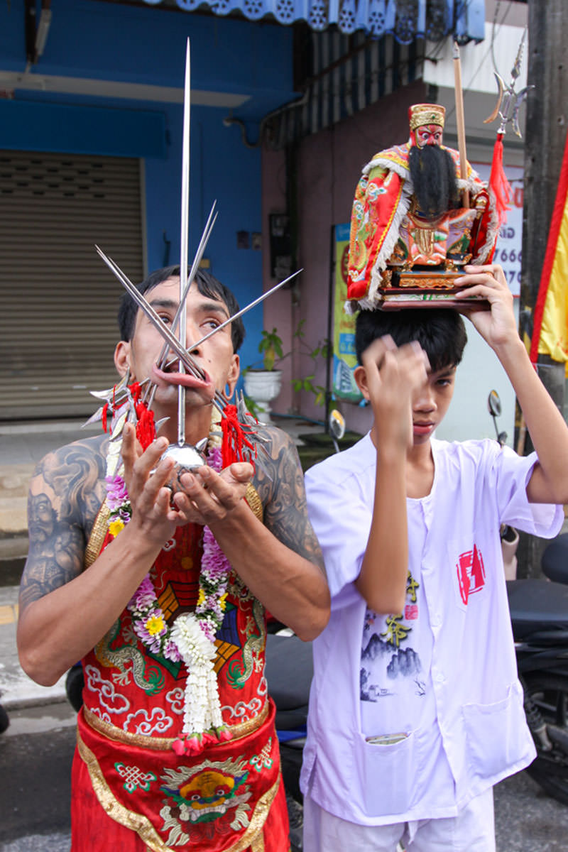 Ma song participant of the Phuket Vegetarian Festival, his face heavily pierced with spikes, standing by the road during the procession of the Lim Hu Tai Su Shrine, Thailand; photo by Ivan Kralj.