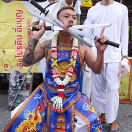 Ma song participant of the Phuket Vegetarian Festival, his face pierced with swords, resting on the side of the road during the procession from the Lim Hu Tai Su Shrine, Thailand; photo by Ivan Kralj.