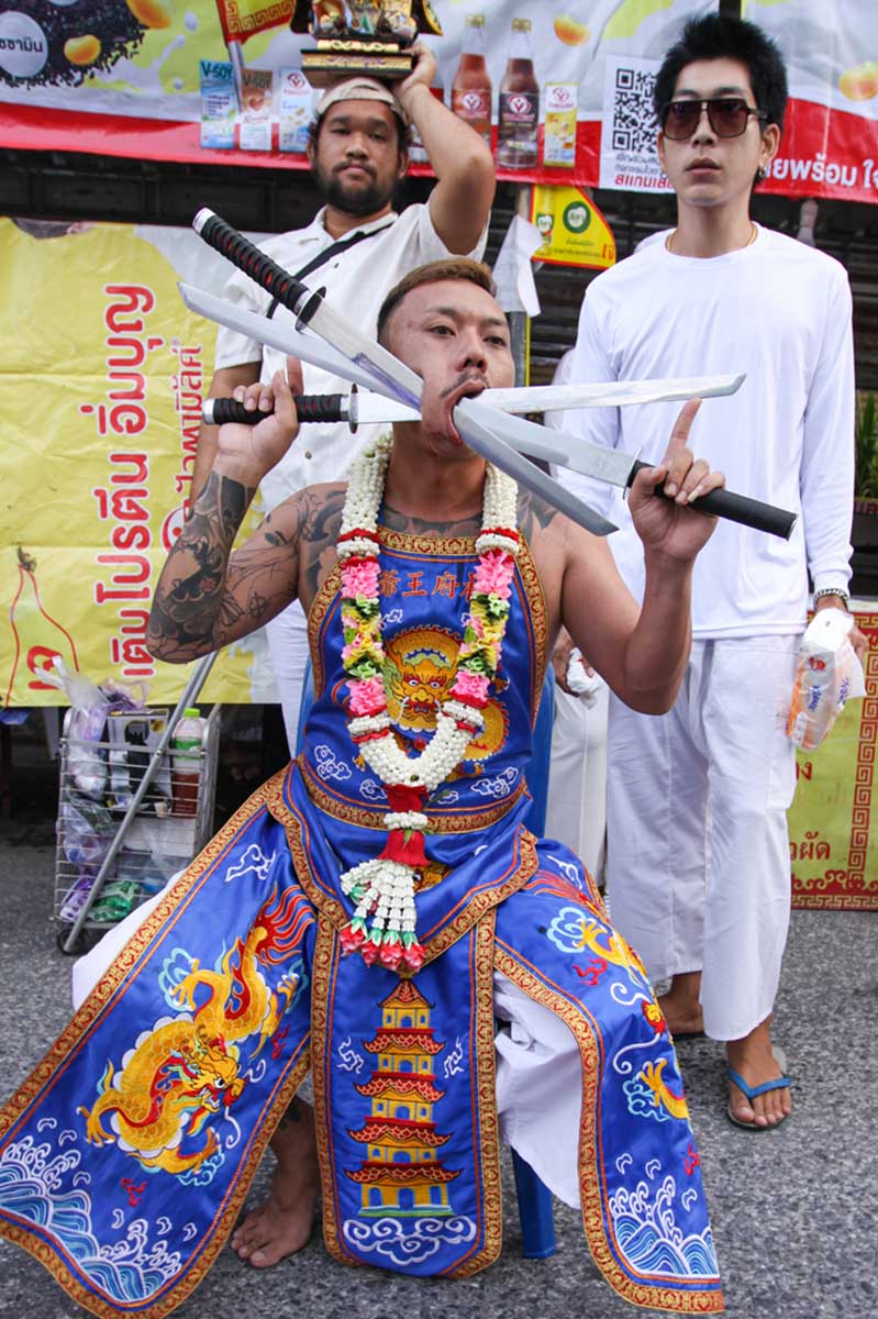Ma song participant of the Phuket Vegetarian Festival, his face pierced with swords, resting on the side of the road during the procession from the Lim Hu Tai Su Shrine, Thailand; photo by Ivan Kralj.