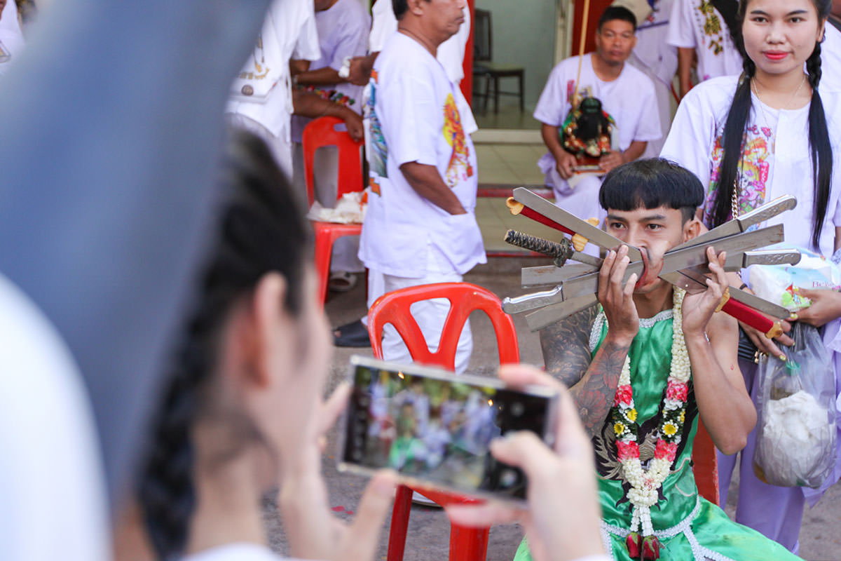 Ma song participant of the Phuket Vegetarian Festival, his cheeks pierced by swords, getting photographed at the Lim Hu Tai Su Shrine, while awaiting the start of the procession; photo by Ivan Kralj.