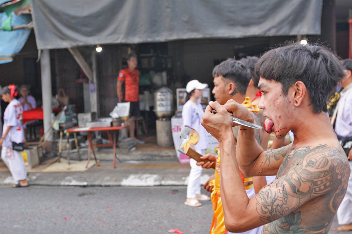 Ma song participant of the Phuket Vegetarian Festival, walking in the procession from the Lim Hu Tai Su Shrine while cutting his tongue with an axe, Thailand; photo by Ivan Kralj.