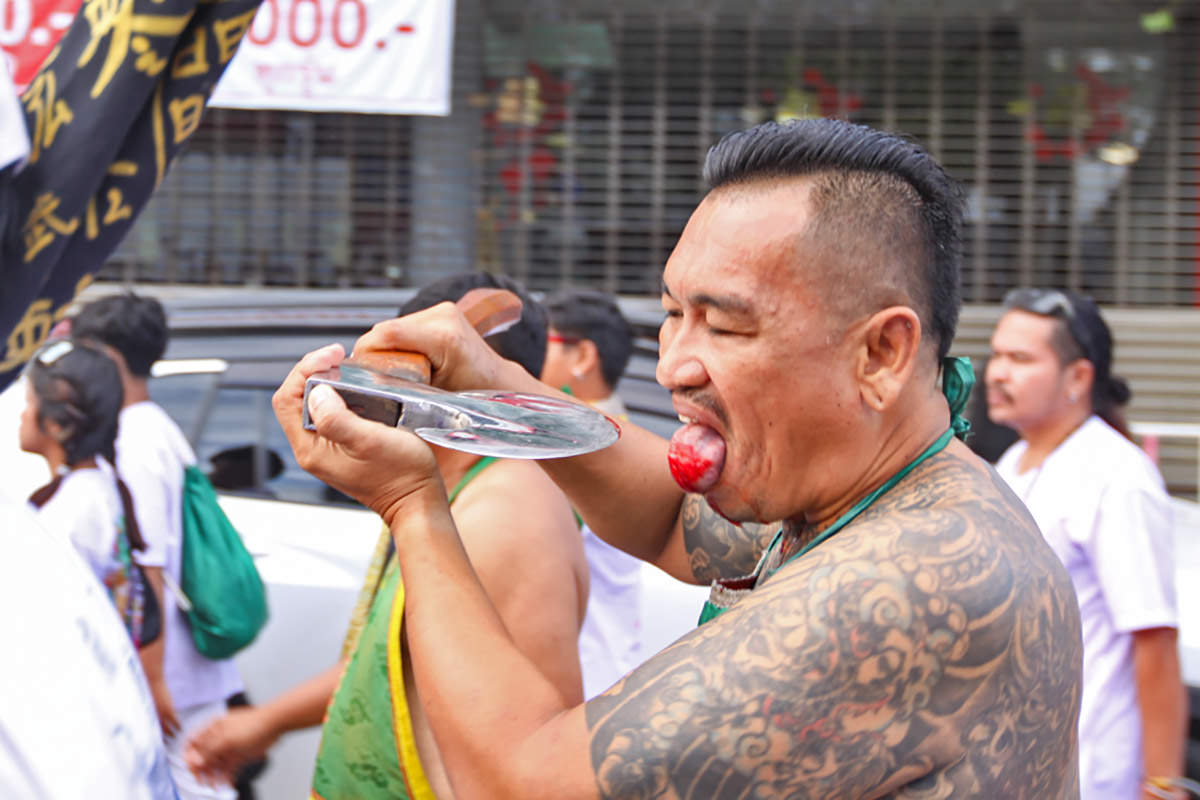 Ma song participant of the Phuket Vegetarian Festival, walking in the procession from the Lim Hu Tai Su Shrine while cutting his bleeding tongue with an axe, Thailand; photo by Ivan Kralj.