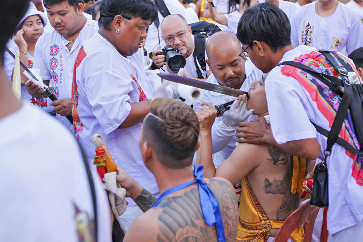 Ma song participant of the Phuket Vegetarian Festival, getting his face cheek pierced by a sword, ahead of the town procession; photo by Ivan Kralj.