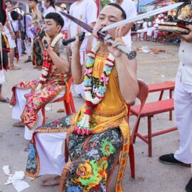 Ma song participants of the Phuket Vegetarian Festival, their cheeks pierced by swords, sitting at the Lim Hu Tai Su Shrine, awaiting the start of the procession; photo by Ivan Kralj.