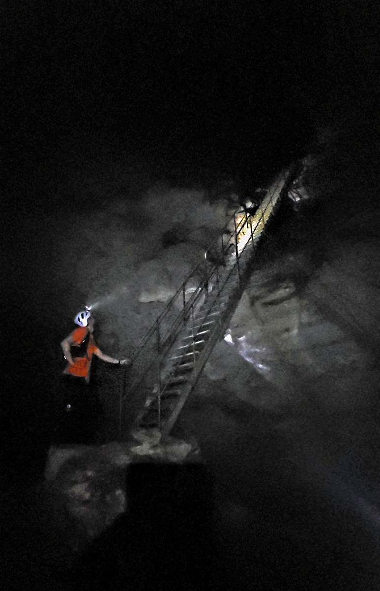 Slovenian tour guide Nejc Prinčič illuminating the steep ladder stairs in the darkness of Predjama Castle Cave with his headlight; photo by Ivan Kralj.
