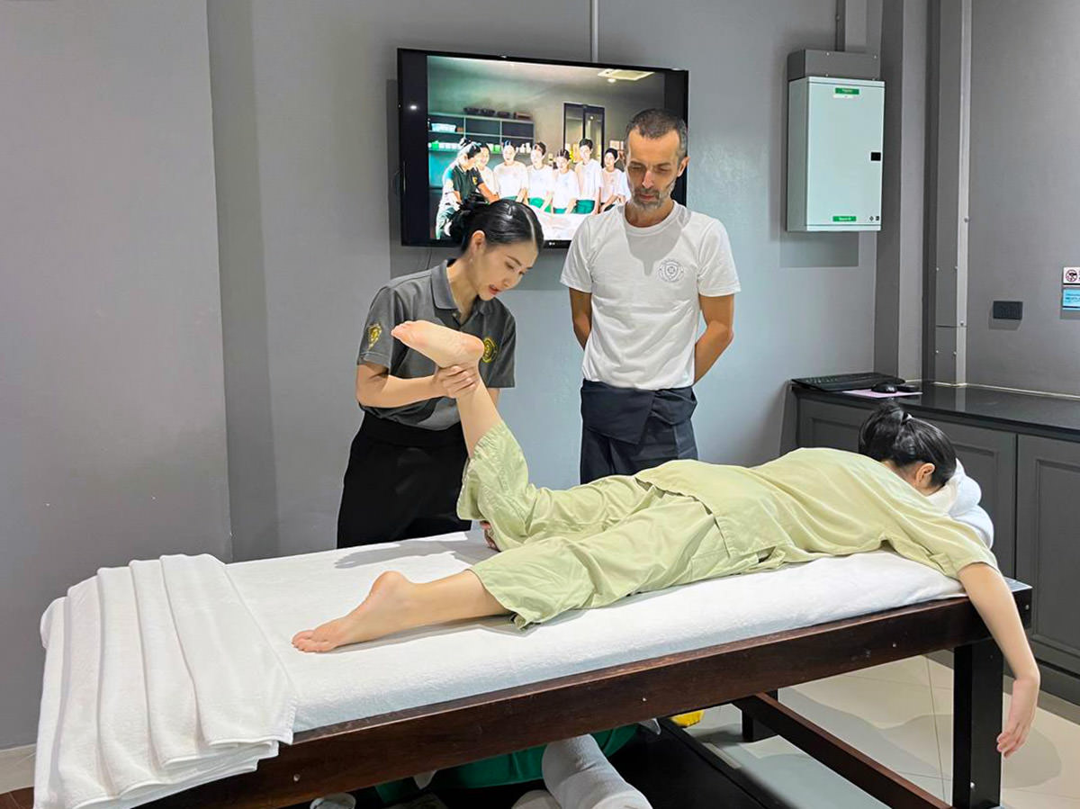 Nigel Amonrat Paojae explaining the principles of the Thai massage to travel blogger Ivan Kralj, while demonstrating on a "customer" at Thai Oasis Spa School in Chiang Mai, Thailand; photo by Ivan Kralj.