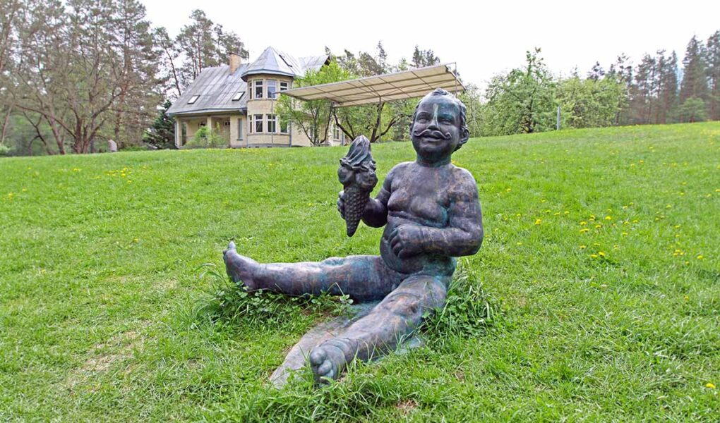 The sculpture of a boy "With Moustaches", holding an ice-cream cone, a work by the Lithuanian sculptor Evaldas Pauza, sitting on the grass at Europos Parkas, an open-air museum at the geographical center of Europe; photo by Ivan Kralj.