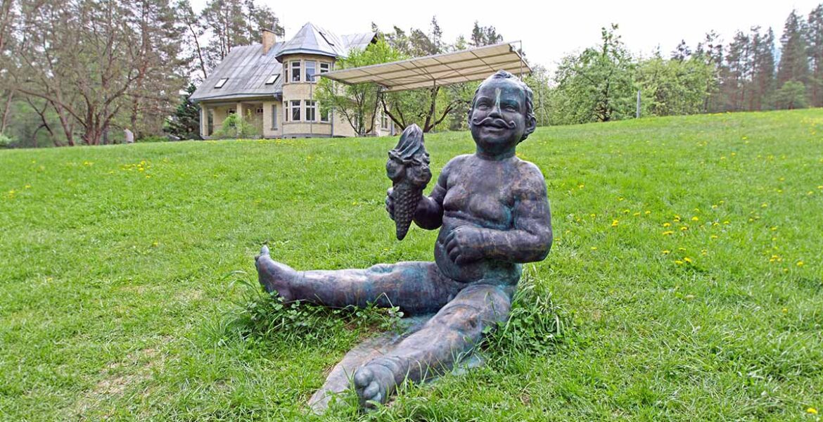The sculpture of a boy "With Moustaches", holding an ice-cream cone, a work by the Lithuanian sculptor Evaldas Pauza, sitting on the grass at Europos Parkas, an open-air museum at the geographical center of Europe; photo by Ivan Kralj.