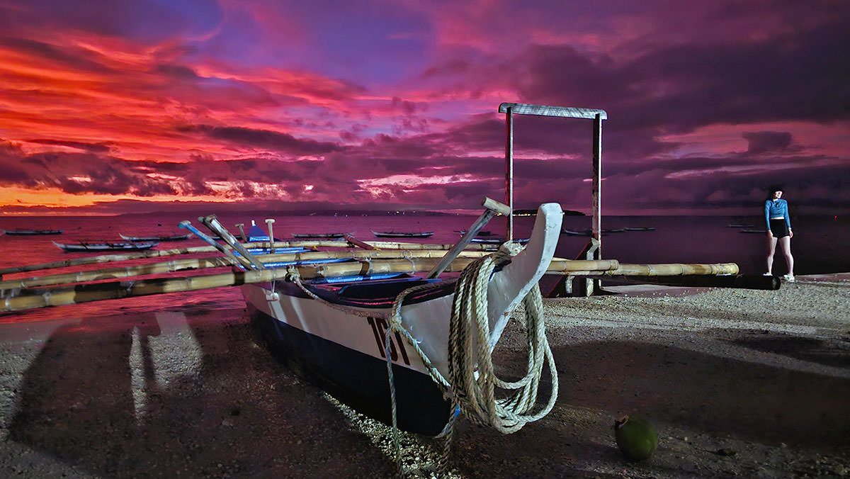 A colorful orange-pin-purple sky above Bohol Sea at sunrise, as seen from Tan-awan barangay, with bangka outrigger boats waiting to take tourists to Oslob whale shark watching experience, Cebu Island, the Philippines; photo by Ivan Kralj.