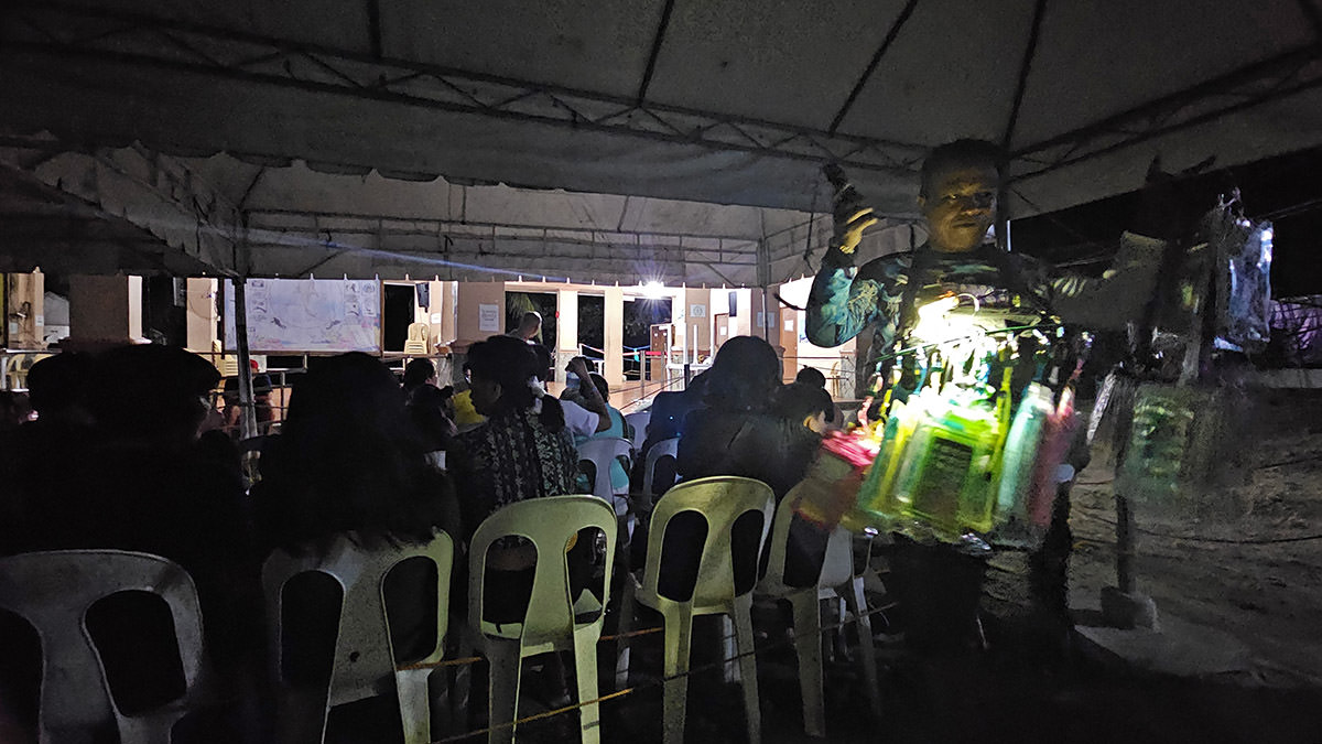 Before dawn, a man selling waterproof mobile phone cases to tourists sitting in the waiting area of the Oslob whale shark watching center, Cebu Island, the Philippines; photo by Ivan Kralj.