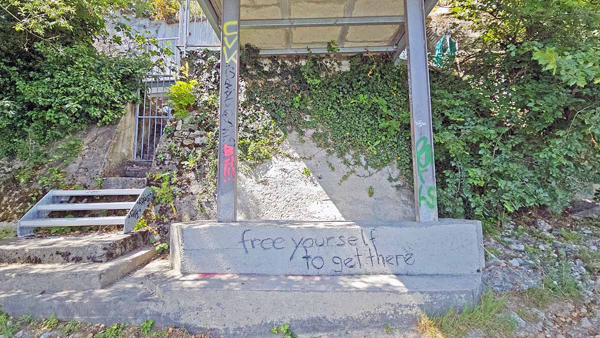 "Free yourself to get there", a graffiti written on the wall under one of the fishing huts on the Rhine River, in the naturist zone in Basel, Switzerland; photo by Ivan Kralj.