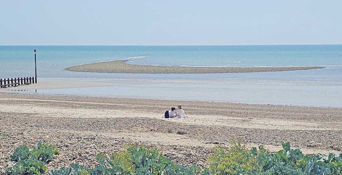 A couple resting alone on the Littlehampton Beach, West Sussex, United Kingdom, with calm sea in the background; photo by Ivan Kralj.