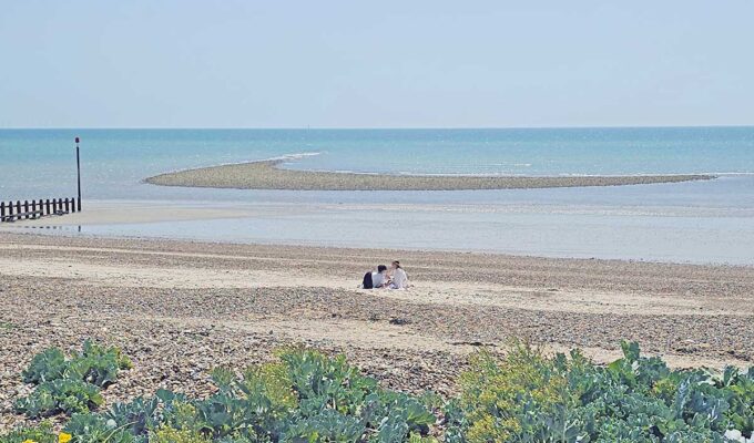 A couple resting alone on the Littlehampton Beach, West Sussex, United Kingdom, with calm sea in the background; photo by Ivan Kralj.