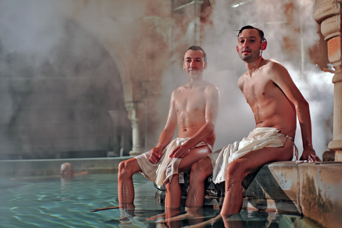 Men sitting by the thermal bath pool in so-called modesty aprons made popular by Rudas Baths in Budapest, Hungary; AI image by Ivan Kralj / Reve.