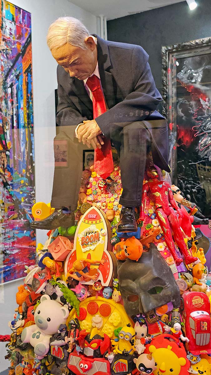 Benjamin Netanyahu sitting atop a mount of colorful toys, a miniature sculpture by Mason Storm asking whether you see a h ero or a villain, displayed in Basel's Galerie Gleis4, Switzerland; photo by Ivan Kralj.